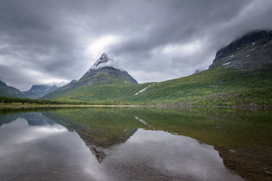Tower of Innerdalen in clouds beautiful peak with reflection in lake Norway