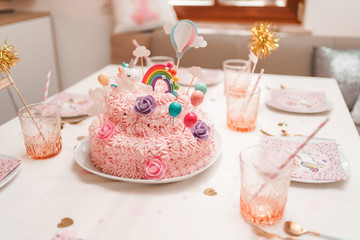 Pink decorated cake with unicorn rainbow flowers and balloons on table for party