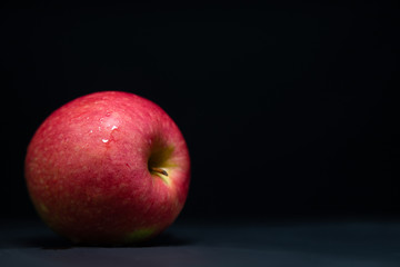 Red apple put on side with water over it look fresh, have light shine on it in dark luxury tone on black background