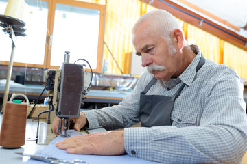 mature specialist stitching shoes on leather sewing machine at factory