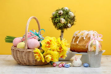 Wicker basket with Easter eggs and bouquet of daffodil flowers.
