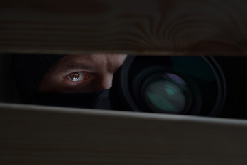 Male eye and camera close-up. Recording to a hidden camera. Private detective with camera looks at a cleft. Espionage background. The concept of eavesdropping, espionage, gossip and the yellow press - obrazy, fototapety, plakaty