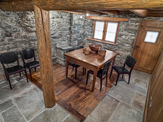 interior shot of a rustic dining room with old table and modern leather chairs the floor and the walls are made of stone