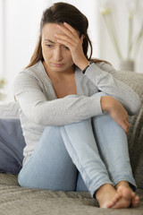 Obraz premium sad woman sitting on sofa at home