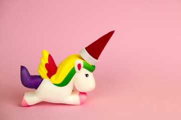squishy unicorn toy with Santa Claus hat  on its horn on a pink background with copy space
