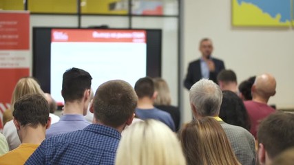 American team leader presenting financial project for people at conference in office interior. Group of employees sitting in training class and listening business coach in room with screen. Concept