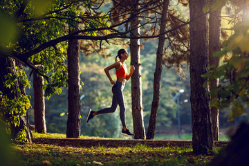 Side view of slim attractive caucasian brunette in sportswear and with ponytail running on trail in...