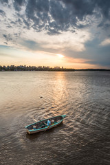 Hombre pescando en canoa en el rio, con un atardecer hermoso de fondo