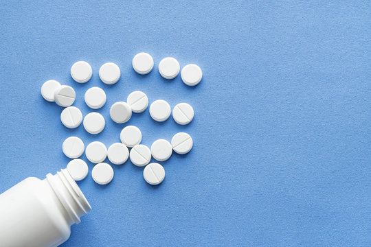 Bottle with white vitamin pills scattered on a blue background.