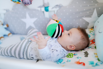 Adorable caucasian little baby boy lying in his crib and playing with stuffed ball.