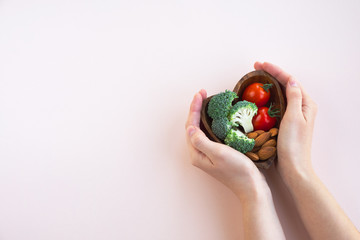 Healthy food for heart on light background. A plate with vegetables and nuts in a woman's hands....