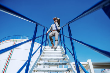 Full length of handsome Caucasian businessman in suit going down the stairs on oil tank storage.