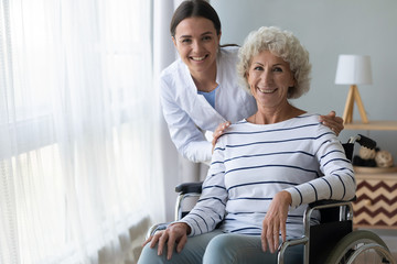 Happy disabled grandma on wheelchair and nurse look at camera