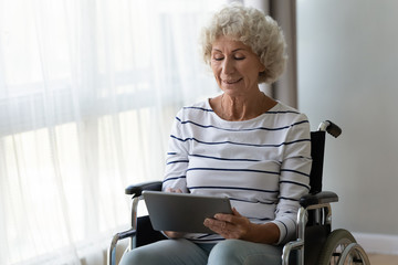 Happy disabled senior woman sit on wheelchair using digital tablet - Powered by Adobe