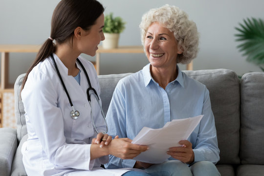 Young woman doctor consult happy old grandmother patient hold papers