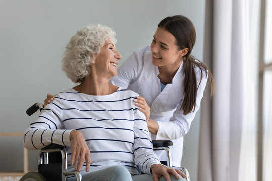 Happy young woman nurse carer help senior grandma on wheelchair