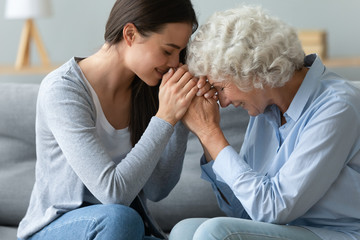 Caring young adult woman granddaughter hold hands of old grandmother