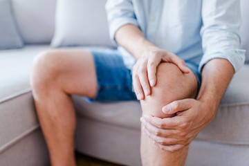 Man suffering from knee pain sitting sofa