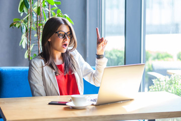 I have an idea. Portrait of surprised beautiful stylish brunette young woman in glasses sitting,...