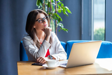 Portrait of thoughtful beautiful stylish brunette young woman in glasses sitting, looking away and...