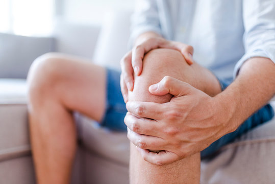 Man suffering from knee pain sitting sofa