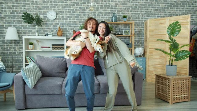 Happy couple man and woman are dancing at home holding corgi dog having fun together enjoying music and animal. Relationship, pets and happiness concept.