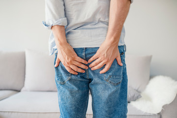 Man holding his bottom in pain, isolated in grey