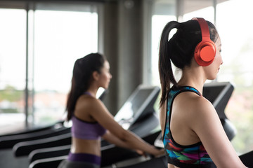 Side View Of Smiling Young Woman Wearing Red Headphones While Exercising On Treadmill In Gym