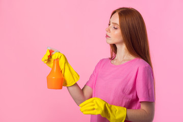 beautiful young woman with red hair in yellow rubber gloves on a pink background