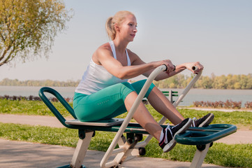 Obraz premium Fit and sporty woman training outside. Girl exercising on a sport machine in outdoor gym.