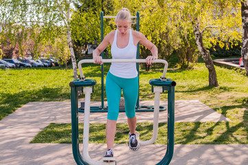 woman exercising with exercise equipment in the public park. Strong girl in training suit working out at outdoor gym. Sport fitness and healthy lifestyle concept.