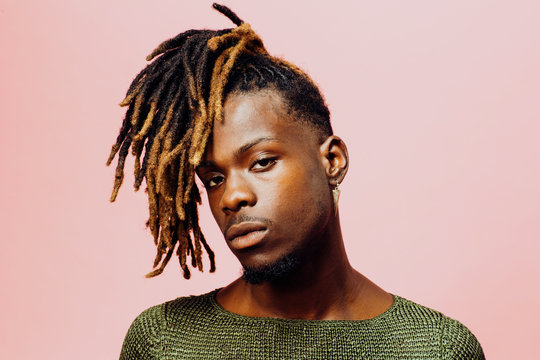 Portrait of a serious  young man in with cool dreadlocks hairstyle, isolated on pink.