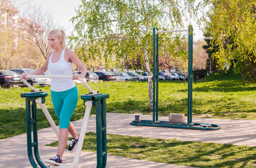 Obraz premium woman exercising with exercise equipment in the public park. Woman in a sports simulator training on the playground outdoors