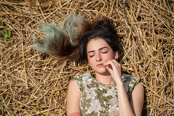 Girl lying in a wheat field and posing on hay dry grass, summer season. Relaxing in nature. Young woman posing in field. Mindset reset