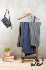 Shopping and style concept - clothes rack with trendy striped pants, blue bag and shoes on wooden floor and grey concrete background