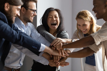 Overjoyed older asian businesswoman joining hands with young multiracial coworkers.