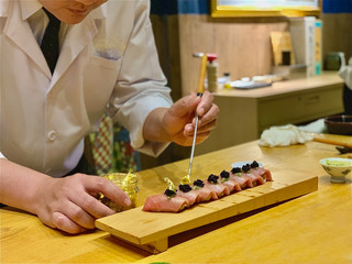 	 Closeup of chef hands preparing japanese food. Japanese Omakase Chef making sushi at restaurant. chef serving traditional japanese sushi with gold served on a stone plate.