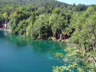 Top view of a quiet azure lake surface surrounded by a mountain forest that densely covers its shores.