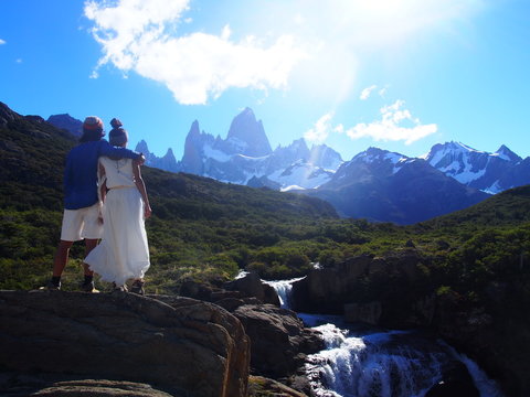 The bride and groom look at Mount Fitz Roy from the banks of a stream in nature, Mountain wedding, Forest wedding, Wedding photoshoot, Los Glaciares National Park near El Chalten, Patagonia, Argentina