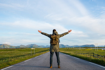 Fototapeta na wymiar Man with backpack walking on an empty road. Amazing landscape, mountain and ocean. Scenic view. New way. Enjoy the moment, relaxation. Wanderlust. Travel, adventure, lifestyle. Explore North Norway
