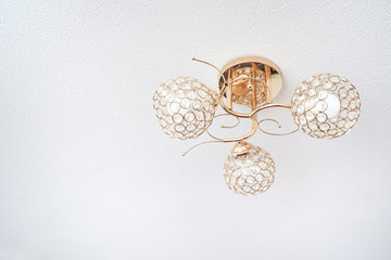 Beautiful ceiling chandelier in gold color in the form of three balls, on a white ceiling background