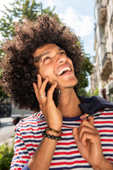 Close up happy cool young arab guy with afro hair talking with mobile phone and looking up