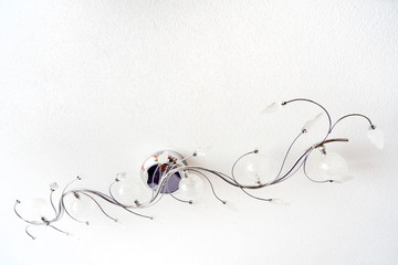 An unusual twisted chrome ceiling chandelier on a white ceiling looks like a branch of a plant