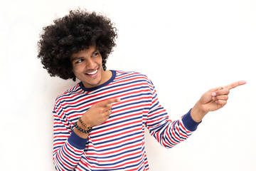 smiling young arab guy with afro hair and pointing fingers to copy space on white background