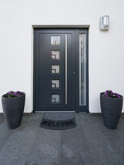 Front door with welcome rug and flowers in a large flower pot