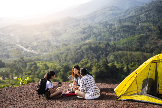 Two Asian Female Hikers Sit And Clinking Glasses By Tent.