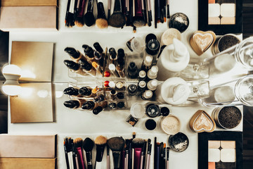On the table with a mirror, are brushes, lipstick, cream, mascara and hair spray in warm colors