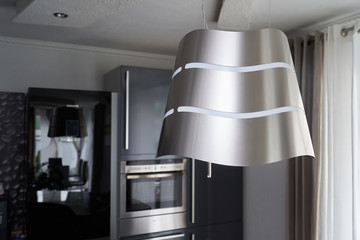 Unusual suspended extractor hood in a metallic color kitchen against the background of kitchen furniture
