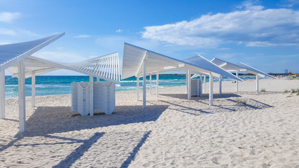 A lot of closed sun loungers on a sandy beach without people on the background of the sea and the sky with white clouds.