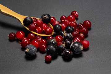 Frozen black currant and cranberries on a wooden spoon.